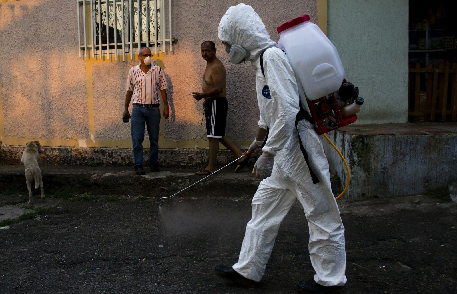 Un fumigador con traje blanco trabaja en una calle de barrio
